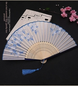 Detail of blue floral silk fan with bamboo hollow ribs and matching tassel on dark desk