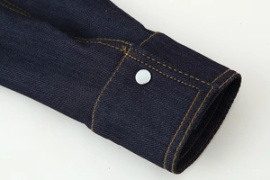 Détail du poignet d'une veste en jean avec coutures orange et bouton argenté