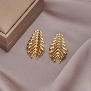 Macro detail of golden leaf-shaped stainless steel earrings on soft velvet texture