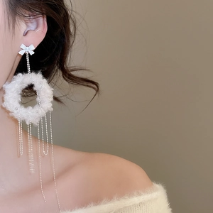 Detailed side view of long plush round tassel earrings with bow knot and silver chains