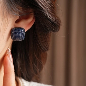 Close-up of pave square stud earrings with dark blue zircon stones on dark metal
