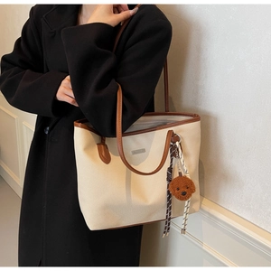 Detail of canvas tote bag with brown leather trim and cute teddy bear charm accessory