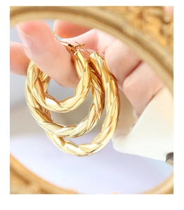 Detailed view of three sizes of gold twisted hoop earrings held against a vintage frame