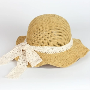 Détail du chapeau de paille kaki clair avec nœud en dentelle blanche et bord ondulé