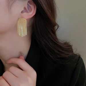 Close-up of gold geometric fringe earrings with vertical texture worn by a model