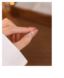 Close-up of minimalist silver teardrop studs held between fingers to show actual scale