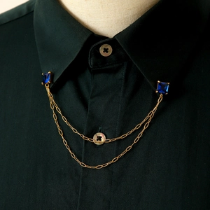 Dettaglio catena per colletto dorata con pietre blu su una camicia nera