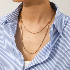 Close-up of a double-layered gold snake chain necklace worn on a striped shirt