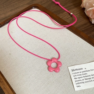 Detailed close-up of a pink flower pendant necklace on a natural wooden tray background
