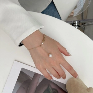 Elegant gold bracelet with delicate pearls and a large pearl pendant on a model's wrist