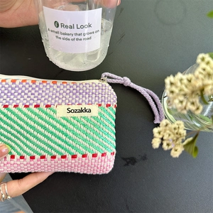 Detailed close-up of a hand-held multi-color striped woven pouch with a zipper lanyard