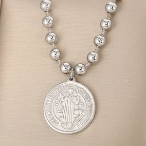 Detail of silver beaded chain necklace with Saint Benedict medal pendant on soft background
