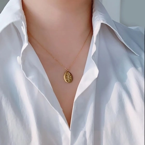 Close-up of golden oval rose pendant necklace worn on white shirt showing vintage detail