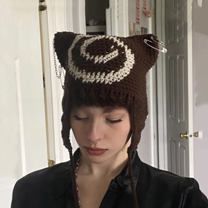Close-up of brown knit cat ear hat featuring white spirals, safety pins, and metal chains