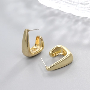 Detailed close-up of polished gold teardrop earrings on a modern grey textured surface