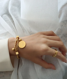 Détail du bracelet doré à double rangée de perles avec un charm rond gravé Love