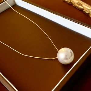 Detailed macro shot of a white round pearl pendant resting in a brown jewelry gift box