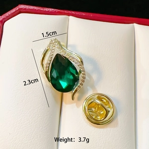 Macro detail of gold flower brooch with green teardrop gem and sizing info