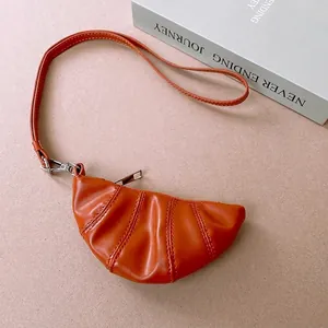Orange croissant neck pouch with quilted pleats and silver zipper on textured background