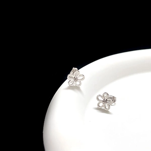 Macro shot of silver titanium flower earrings on a white ceramic plate with black background