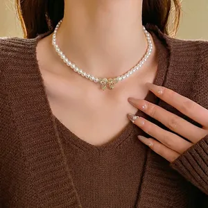 Elegant pearl necklace with a diamond-encrusted gold bow pendant on a female model