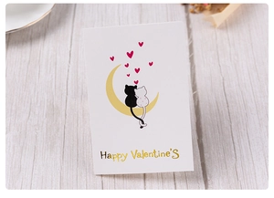 Detail of a white Valentine greeting card with gold foil text and cats sitting on a yellow moon