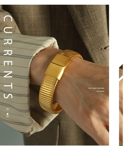 Detail of gold wide cuff bracelet with horizontal textures worn with a brown blazer suit