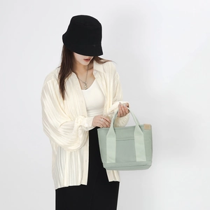 Detail of mint green canvas tote bag with leather tag held by a model in white blouse
