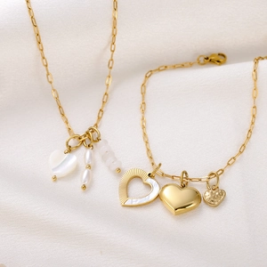 Detailed shot of golden heart necklace and bracelet with shell inlay and pearls on silk