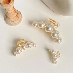 Detailed comparison of pearl hair claws in small, medium, and large sizes on wood stand