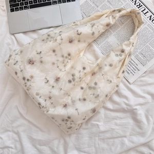 Top view of cream tulle tote bag with floral embroidery near a silver laptop and newspaper