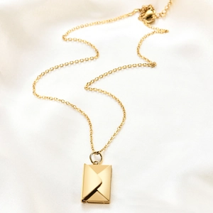 Polished golden stainless steel envelope pendant necklace on elegant white silk fabric