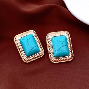 Macro shot of turquoise stone earrings with textured gold metal frame on velvet