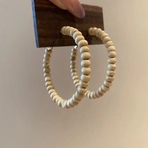 Detail of wooden beaded hoop earrings held on a dark vintage stand in natural soft light