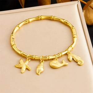 Macro detail of gold bamboo bangle with starfish, shell, and whale charms on silk