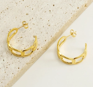 Detail of 18K gold-plated interlocking chain earrings on a textured stone surface