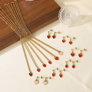 Flat lay of multiple gold titanium necklaces with red and pink strawberry enamel pendants
