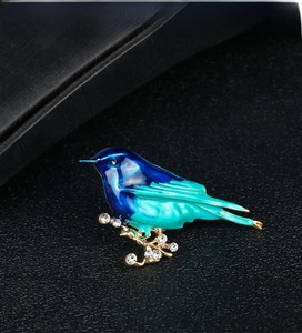 Macro detail of bird brooch with blue enamel wings and clear crystals on golden branch
