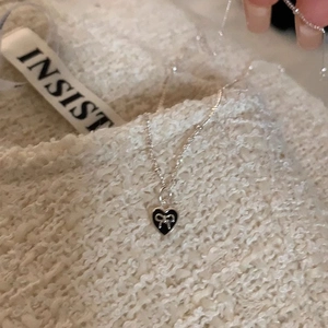 Silver bead chain necklace with black heart and bow pendant on beige knit background