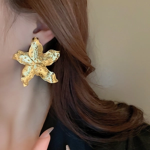 Close-up of golden fan-shaped flower earrings with detailed textured metal finish