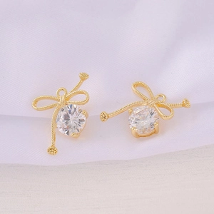 Close-up of gold-plated bow jewelry pendants with clear zircon stones on white fabric