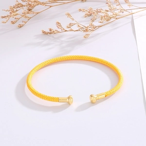 Detail of yellow braided open cuff bracelet with gold metal ends on white background