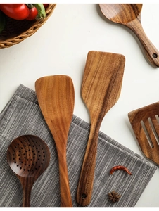Detailed view of handmade teak wood cooking utensils set with natural grain on white tabletop