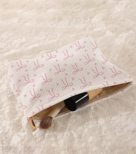 Top view of beige corduroy makeup bag with pink bow print on white lace background