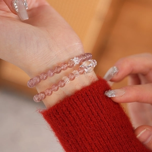 Detail of double-layer strawberry quartz beaded bracelet with crown and bow charms on wrist