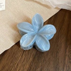 Gros plan sur la pince à cheveux fleur en acrylique bleu marbré sur une table en bois