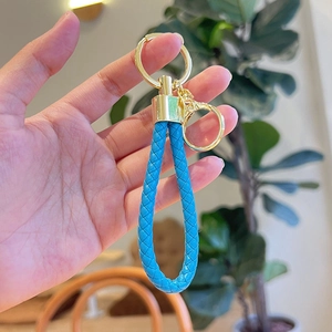 Blue braided leather keychain with gold metal ring and clasp held in hand