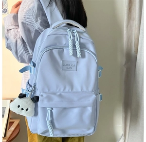 Close-up of light blue nylon backpack with dual zippers and a white puppy pendant