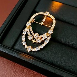 Détail d'une broche ovale plaquée or 18 carats avec zircons et chaînettes