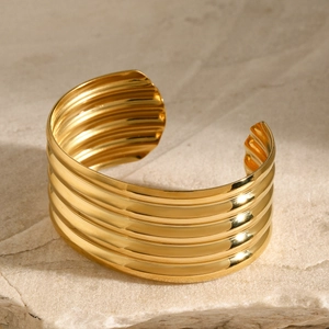 Detail of 18k gold plated stainless steel layered wavy open bangle with polished finish